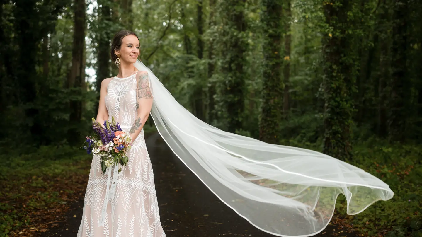 Cyndel en robe de mariée, le voile emporté par le vent en forêt